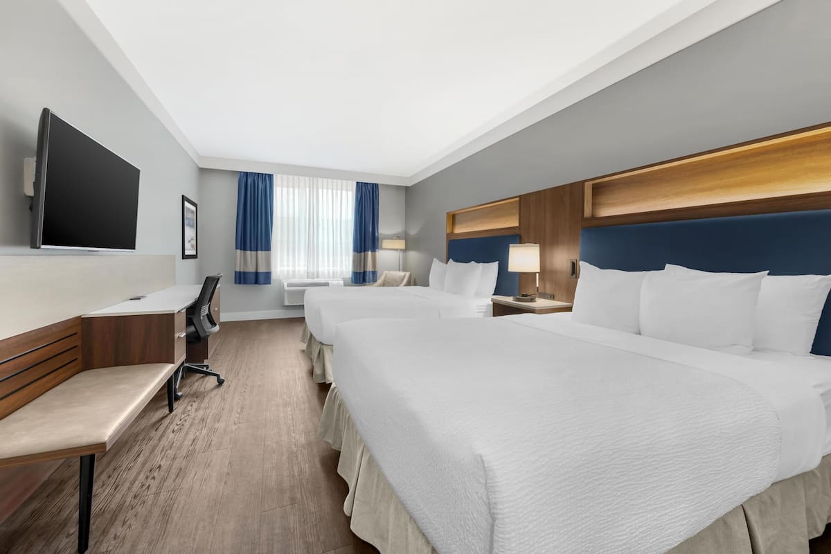 A hotel room with two beds, a desk, a chair, a TV, and a window with curtains.