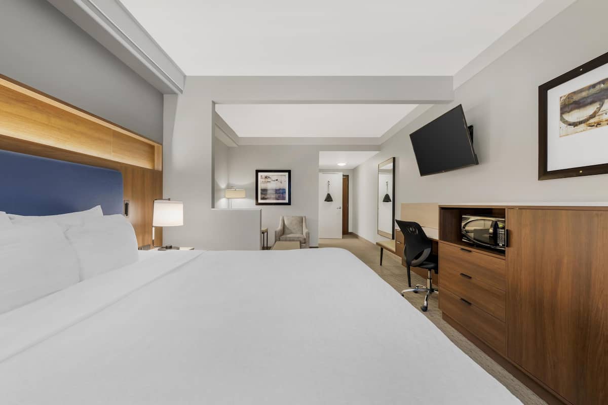 Une chambre d’hôtel avec un grand lit, un bureau avec une chaise, un téléviseur fixé au mur et un tableau encadré au-dessus du bureau.