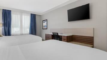 A hotel room with two beds, a desk, a chair, a TV, and a window with curtains.