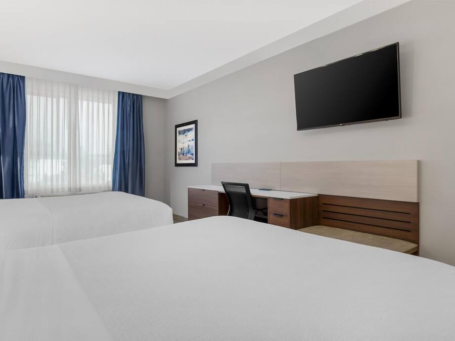A hotel room with two beds, a desk, a chair, a TV, and a window with curtains.