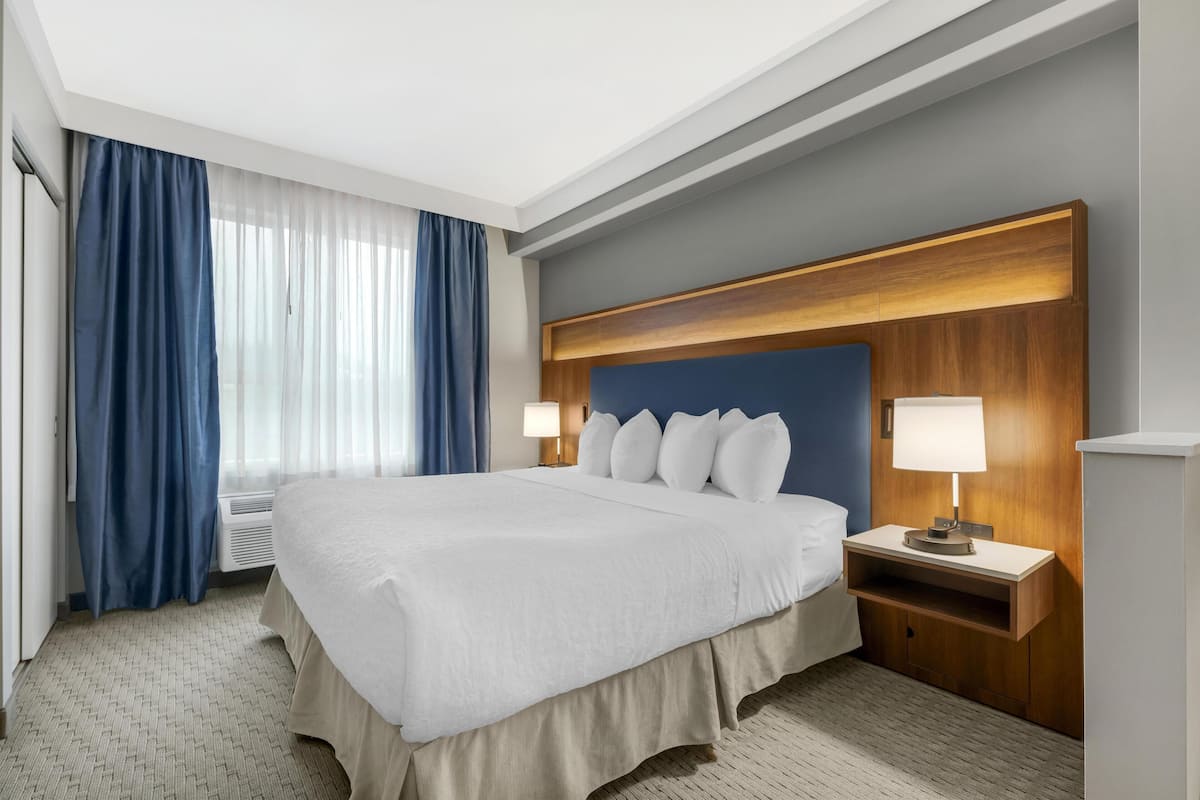 A hotel room with a large bed, a wooden headboard, two bedside tables with lamps, and a window with curtains.