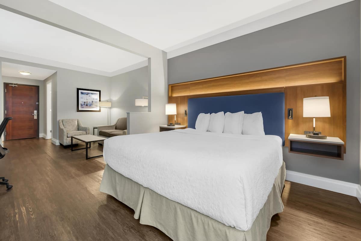 A modern hotel room with a large bed, a desk, a chair, and a small table.