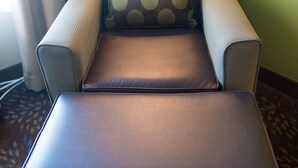 Una habitación con sofá, reposapiés, lámpara y cortina.