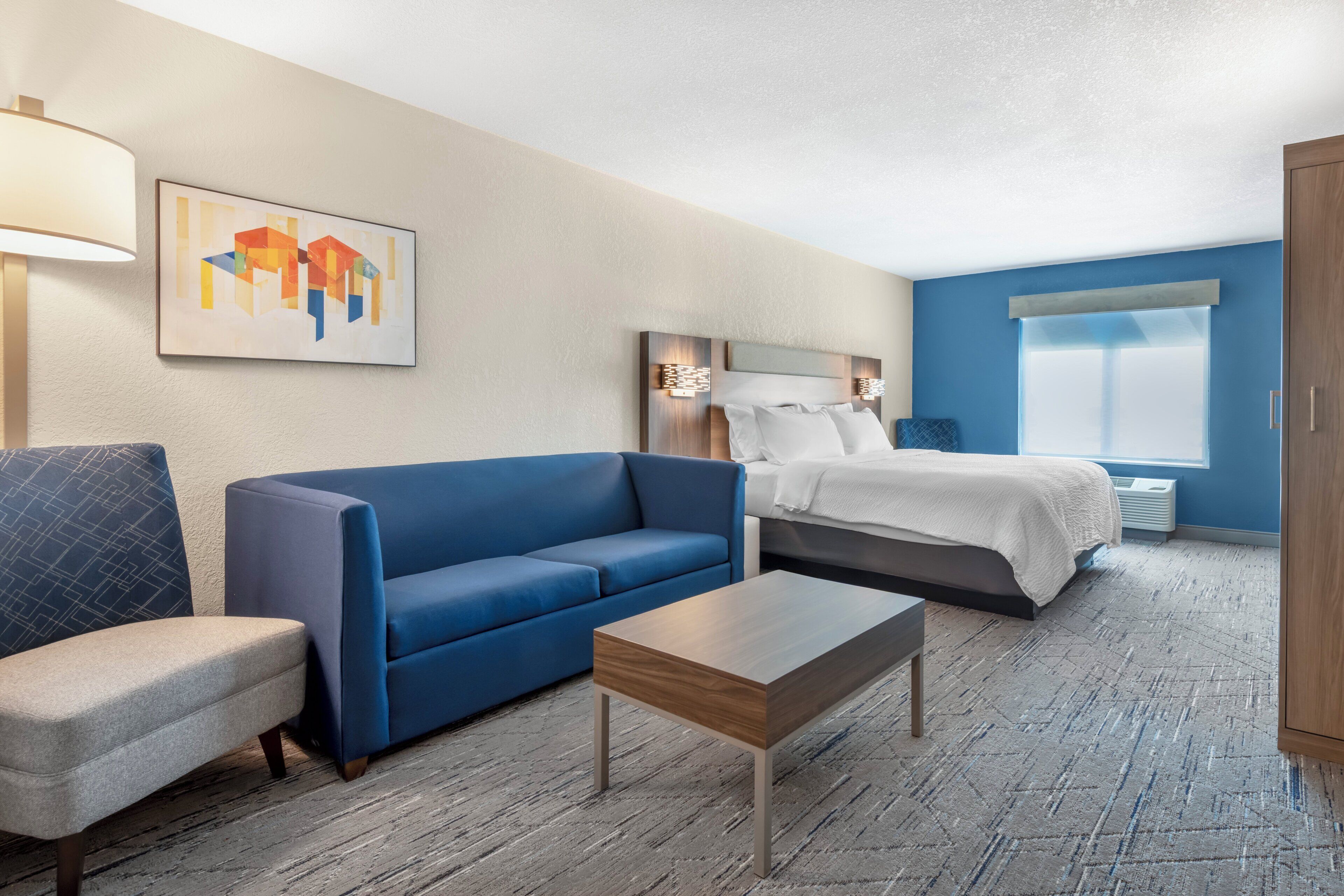 Ein Hotelzimmer mit Bett, Sofa, Sessel, kleinem Tisch und einem Bild an der Wand.