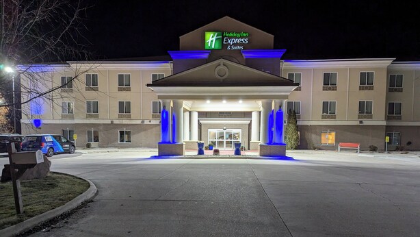 Entrada de un hotel Holiday Inn Express & Suites con un cartel llamativo, un acceso cubierto y un área de estacionamiento.