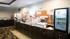Zona de bufé con distintas estaciones de comida, incluyendo un mostrador para huevos y un refrigerador con yogures.