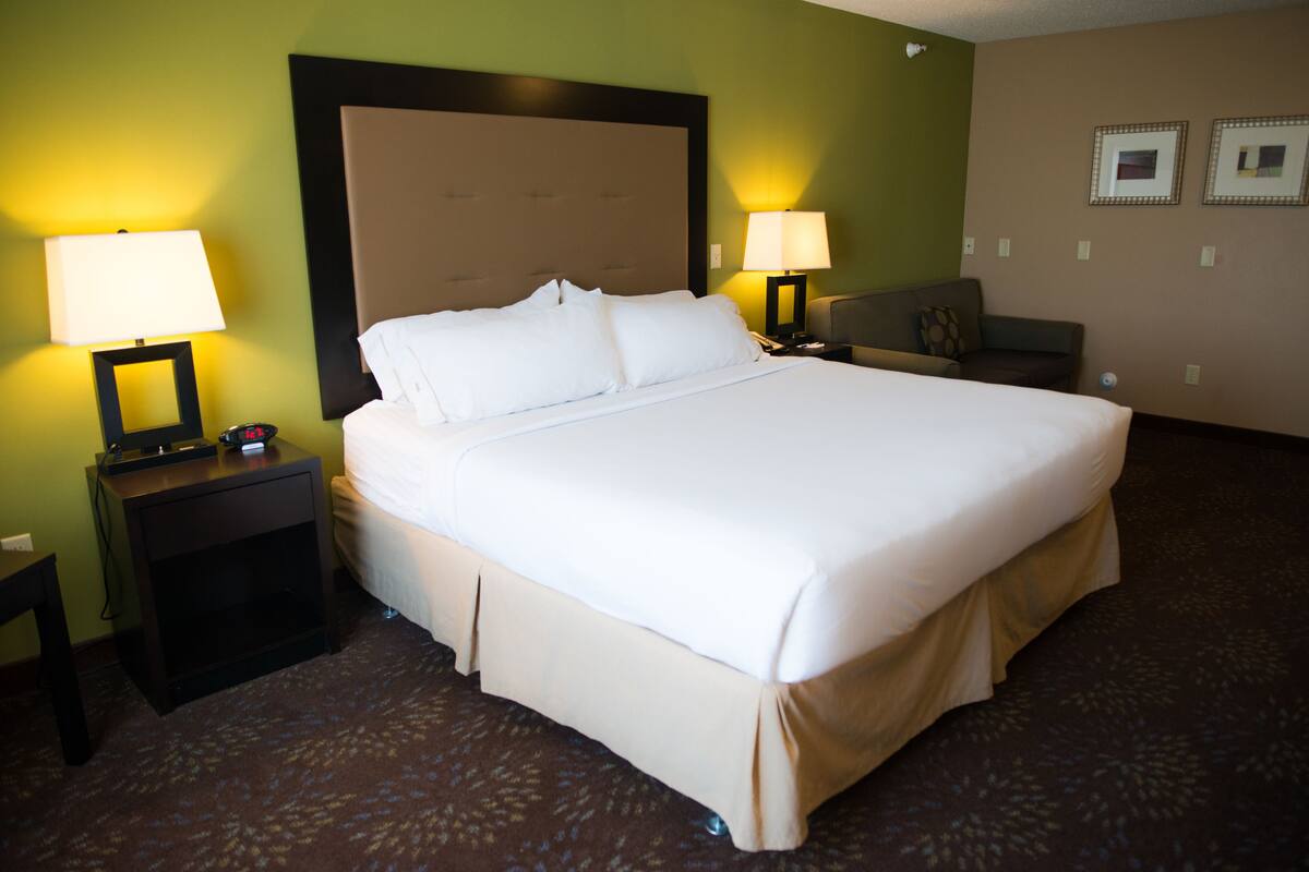Habitación de hotel con una cama grande, dos mesitas de noche con lámparas, un pequeño sofá y piso alfombrado.
