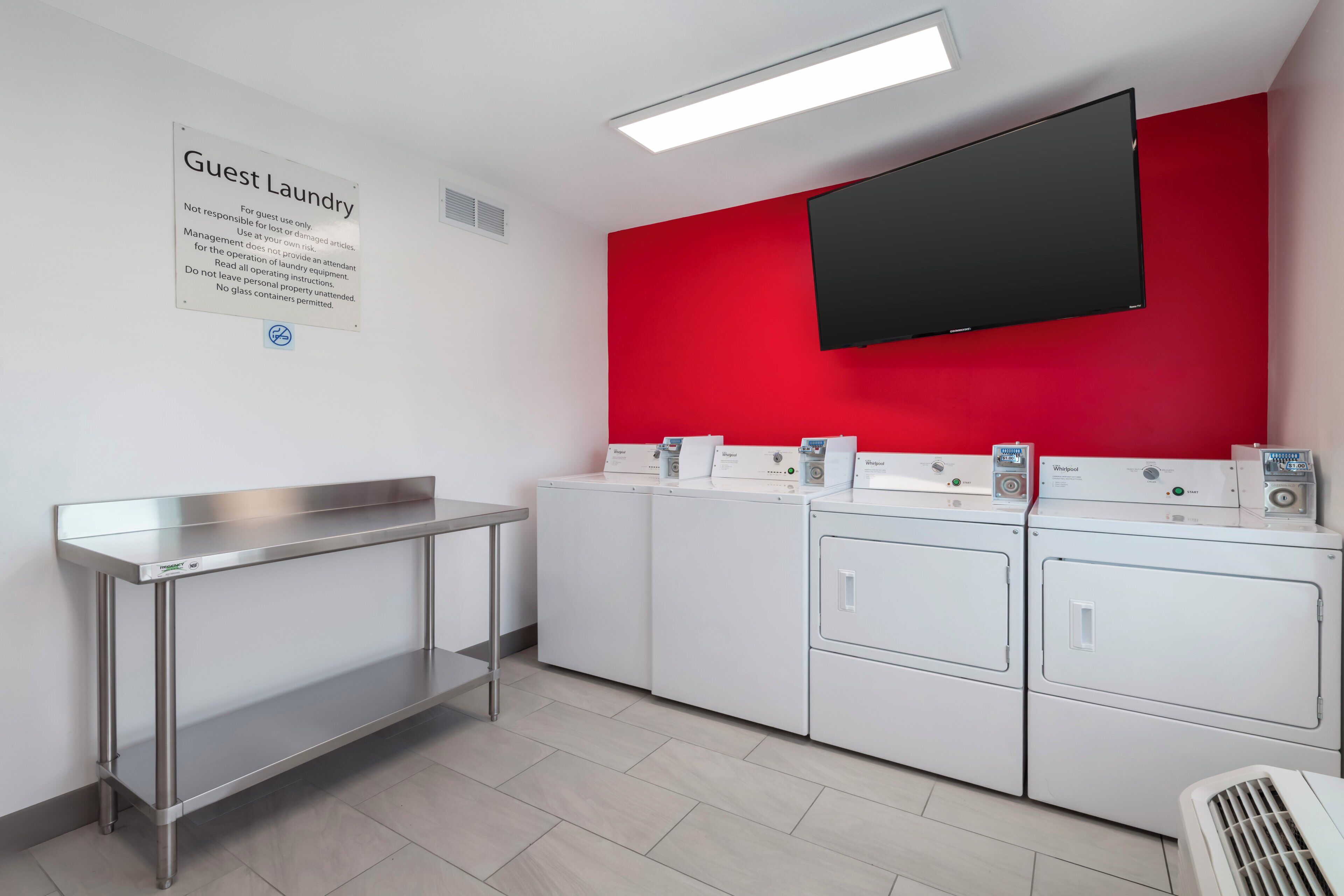 Zona de lavandería con letrero exclusivo para huéspedes, una mesa de acero inoxidable y varias lavadoras Whirlpool.
