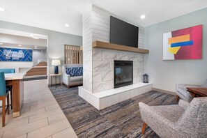 Una sala de estar moderna con chimenea, un comedor con mesa azul, y una cocina al fondo.