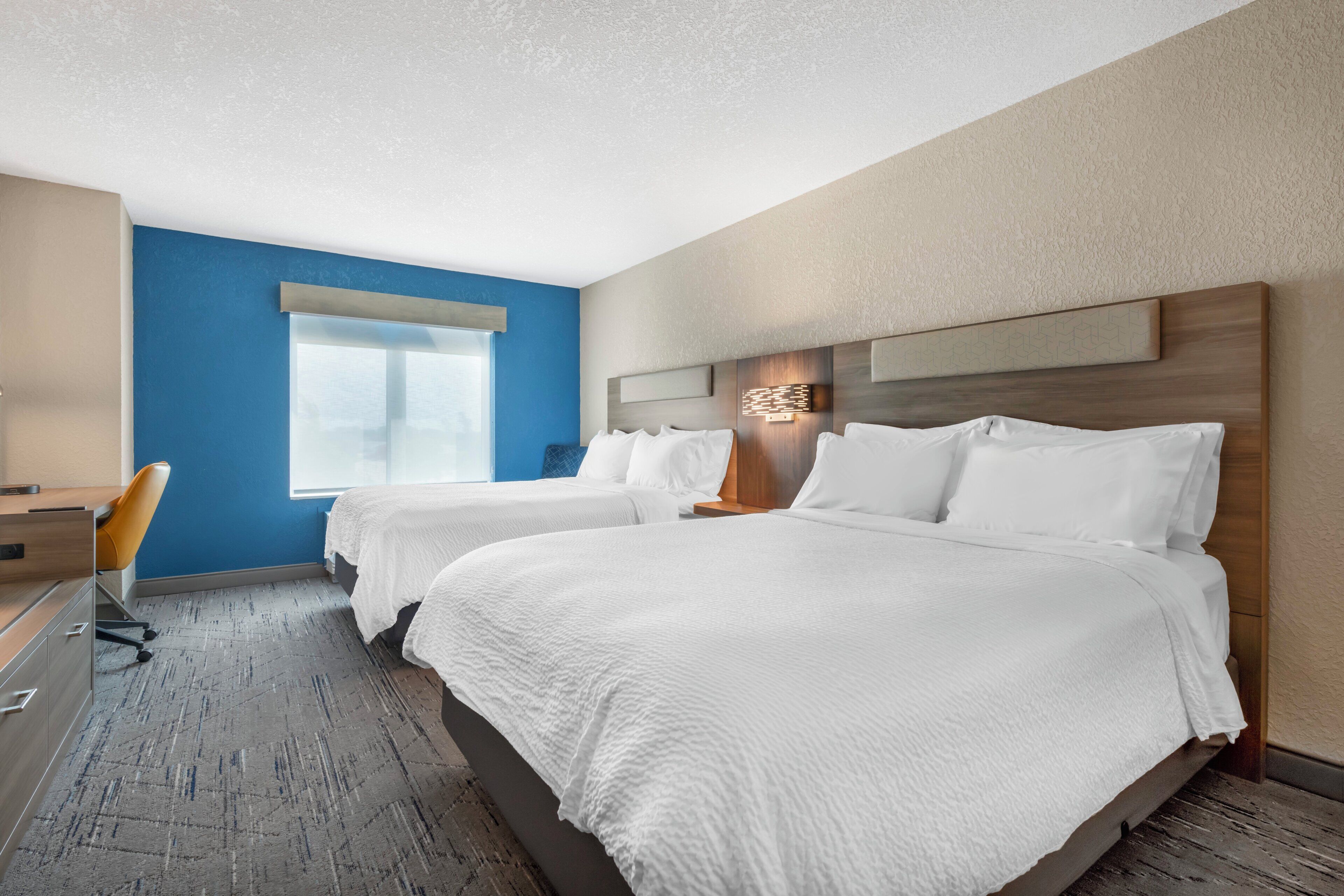A hotel room with two beds, a desk, and a chair.