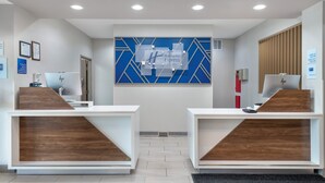 Un área de recepción con dos mostradores, un diseño de pared geométrico azul y un letrero de registro de entrada y salida.