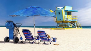 A beach scene with a lifeguard tower, beach chairs, a stroller, and a blue umbrella.