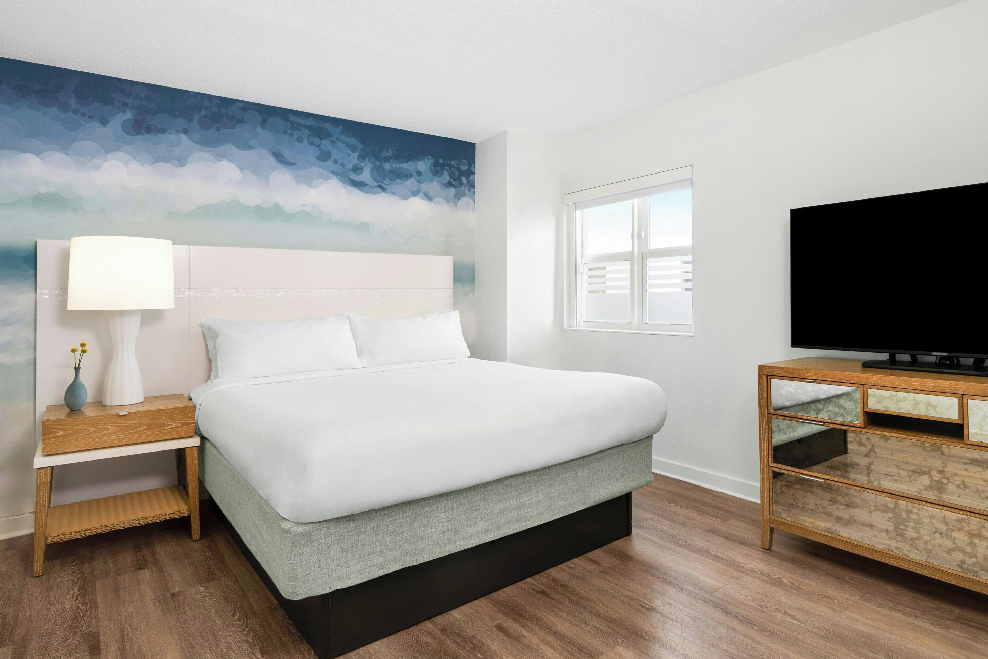 Een moderne hotelkamer met een groot bed, een nachtkastje, een televisie op een houten kast en een muurschildering.