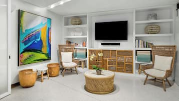 A modern living room with a large abstract painting, wicker furniture, a flat-screen TV, and a bookshelf.