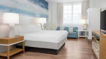 Ein Hotelzimmer mit einem großen Bett, zwei Nachttischen mit Lampen, einem Fernseher, einem Sofa und einem großen Fenster mit Vorhängen.