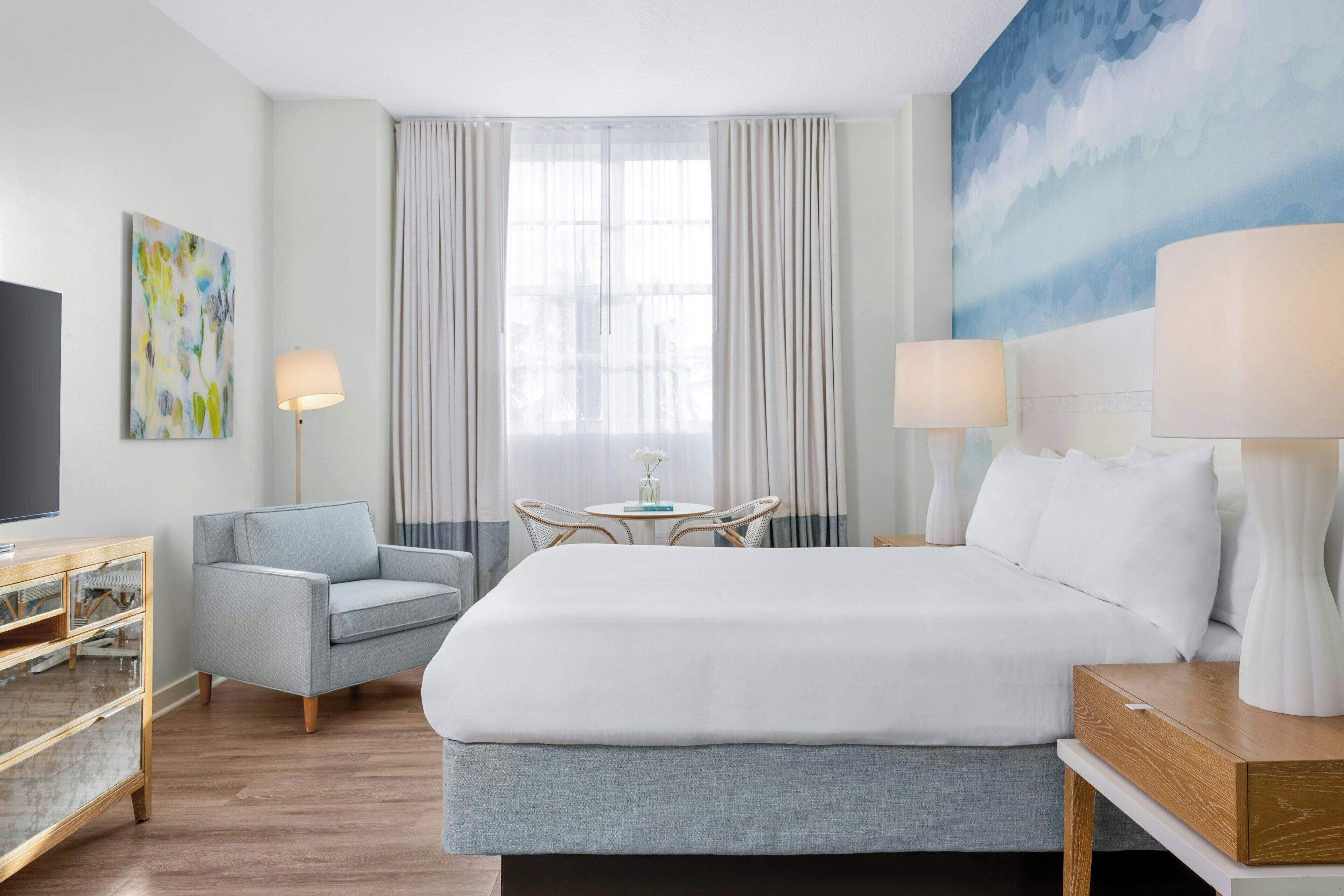 Une chambre d’hôtel avec un grand lit, un coin salon avec une table et un téléviseur posé sur une commode en bois.