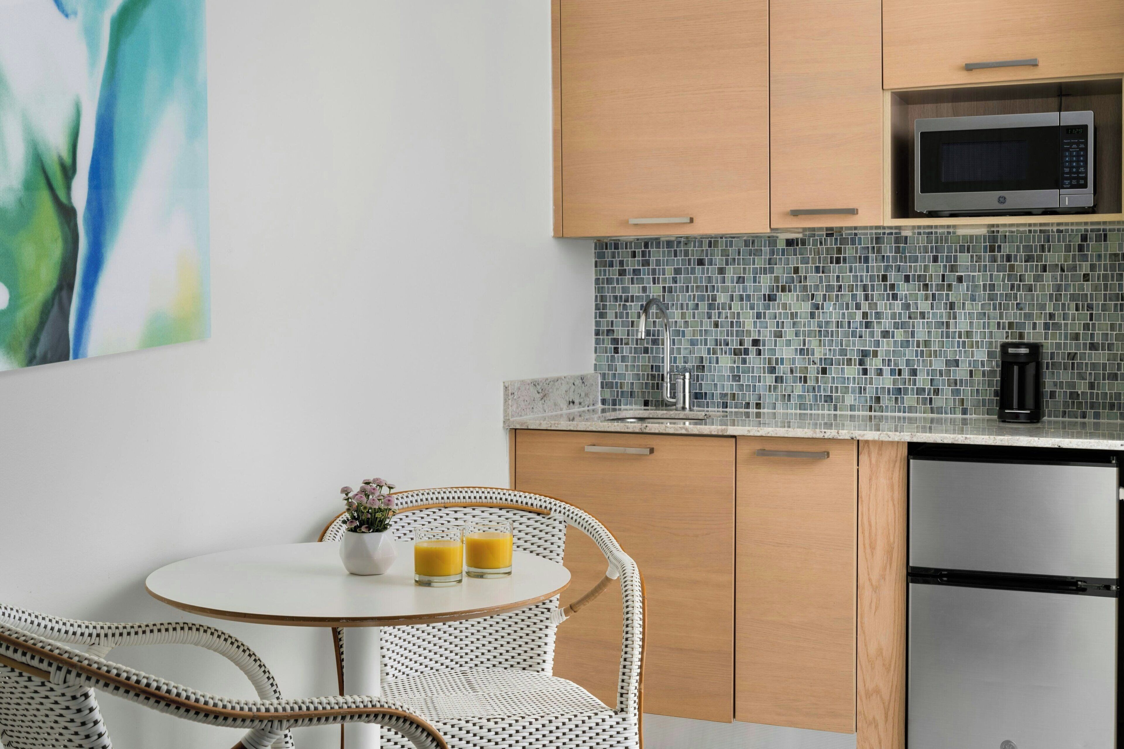 A modern kitchen with wooden cabinets, a stainless steel refrigerator, a microwave, and a tiled backsplash.