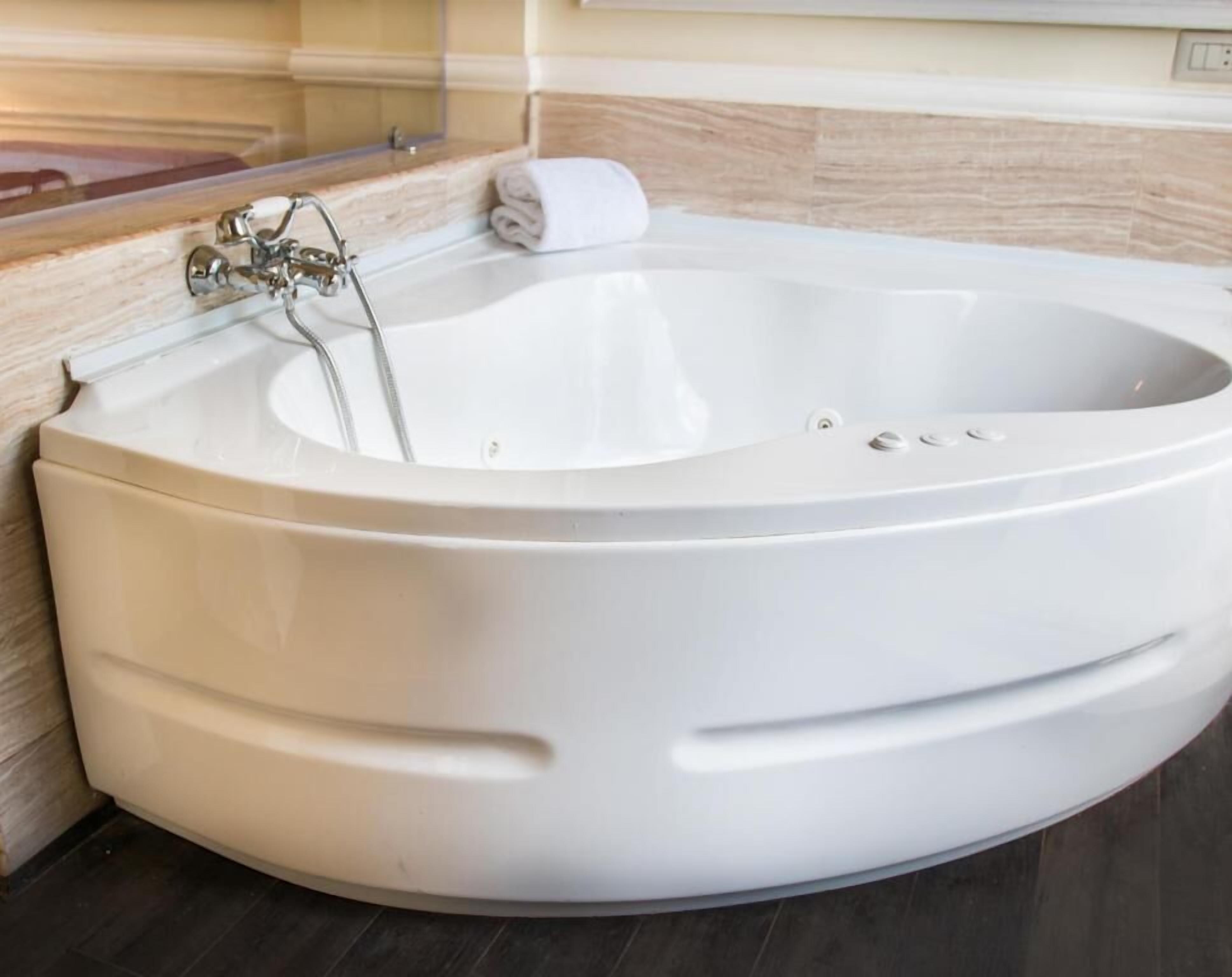 A large, white, freestanding bathtub in a bathroom with a wooden vanity and a towel on the edge.