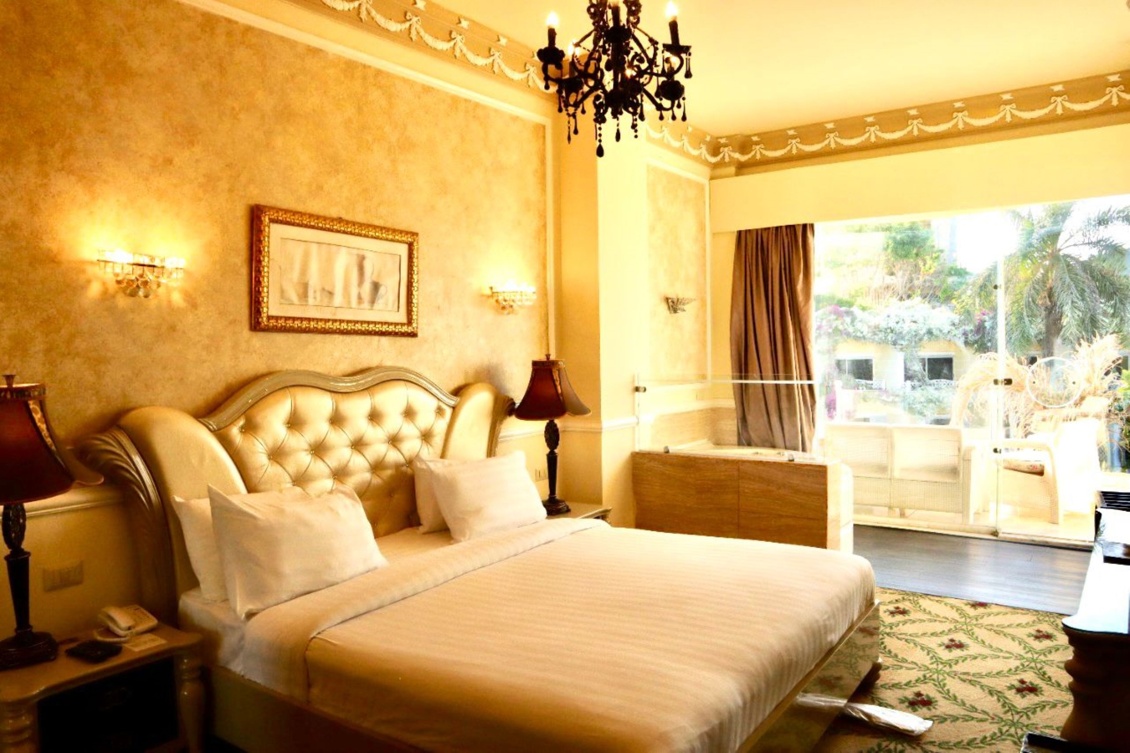 A hotel room with a large bed, a chandelier, and a view of the outdoors.