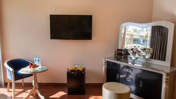 A room with a TV mounted on the wall, a small round table with a chair, a cabinet with drawers, and a large mirror.