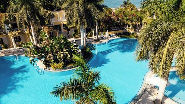 A large, clear blue pool surrounded by palm trees and lounge chairs, with a view of a building in the background. - Paradise Inn Beach Resort - Maamoura (Alexandria)