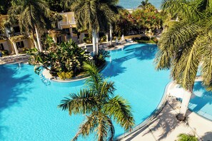 A large, clear blue pool surrounded by palm trees and lounge chairs, with a view of a building in the background. - Paradise Inn Beach Resort - Maamoura (Alexandria)