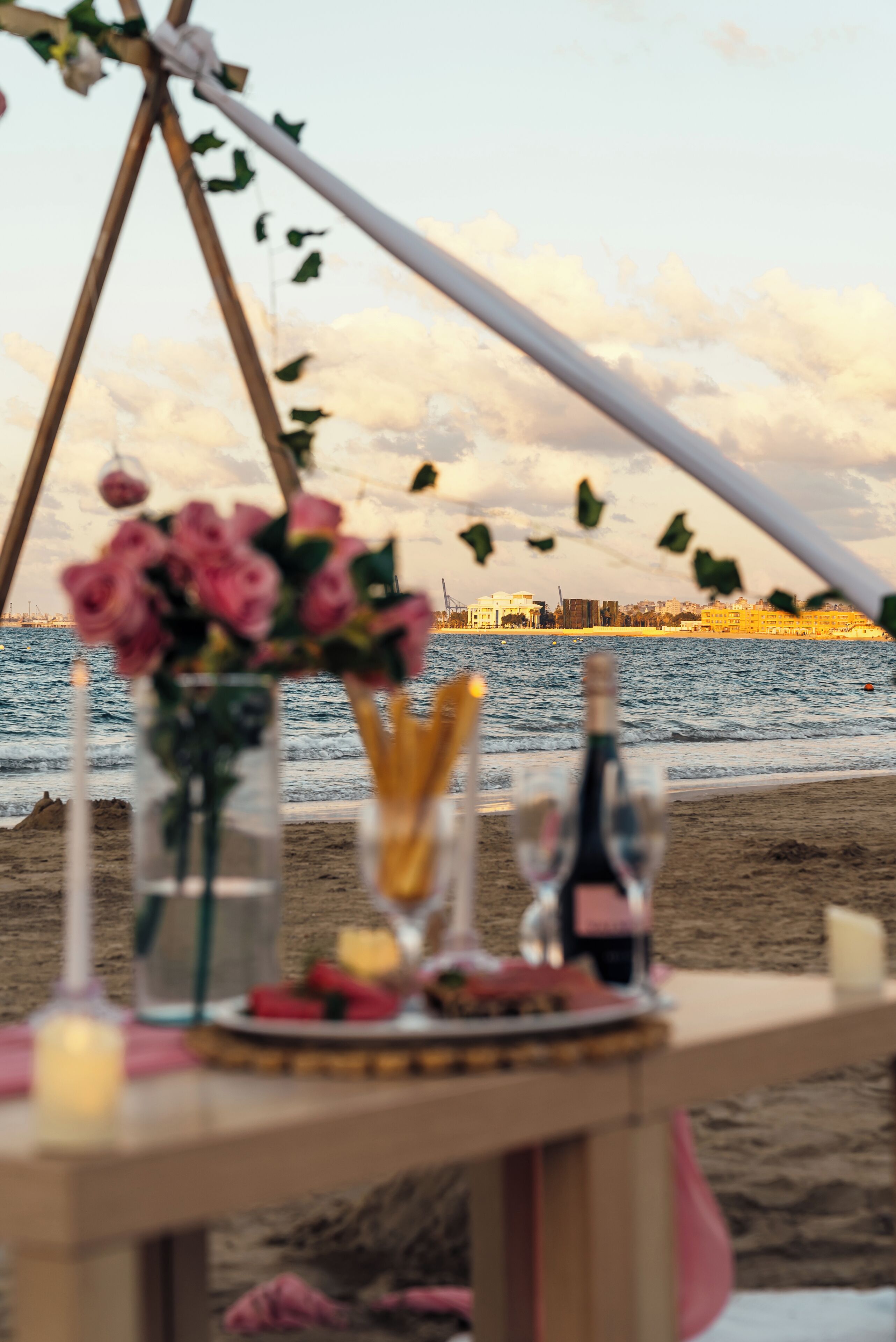 A beachside table with a bottle, glasses, and food, overlooking the sea.