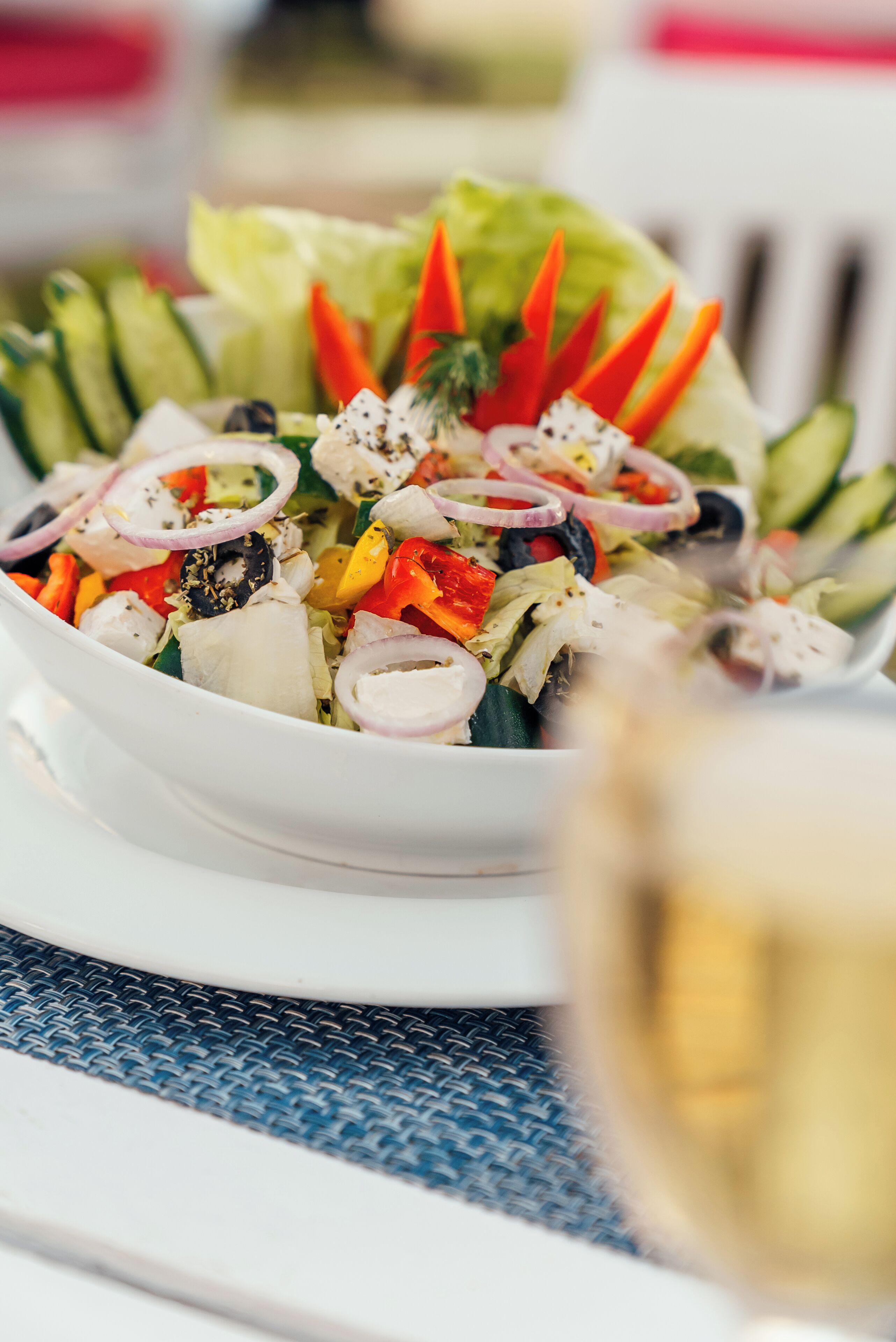 A bowl of salad with various vegetables and a glass of white wine on a table.
