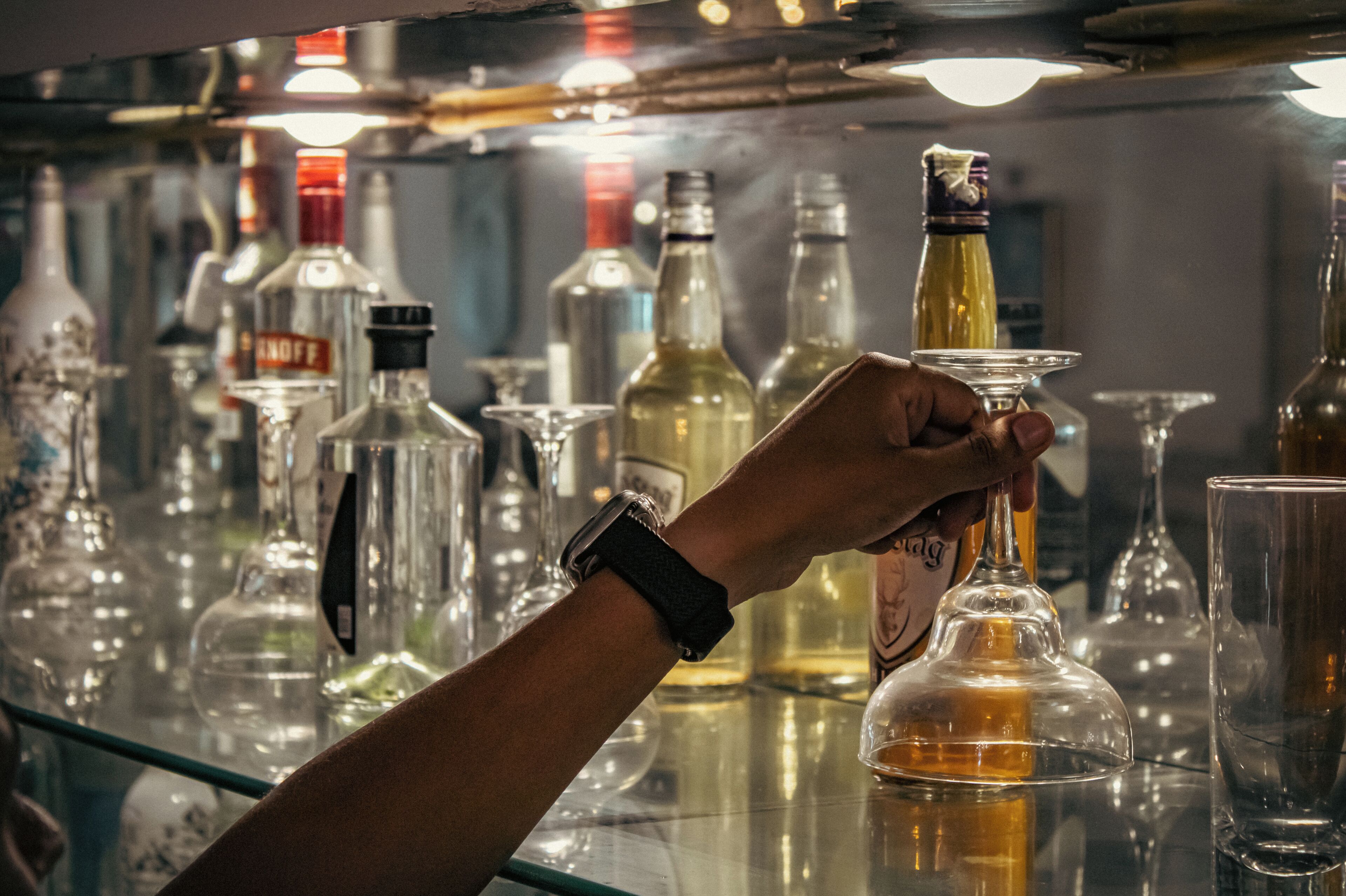 Una mano sosteniendo una botella de licor en un bar, con varias botellas y vasos al fondo.