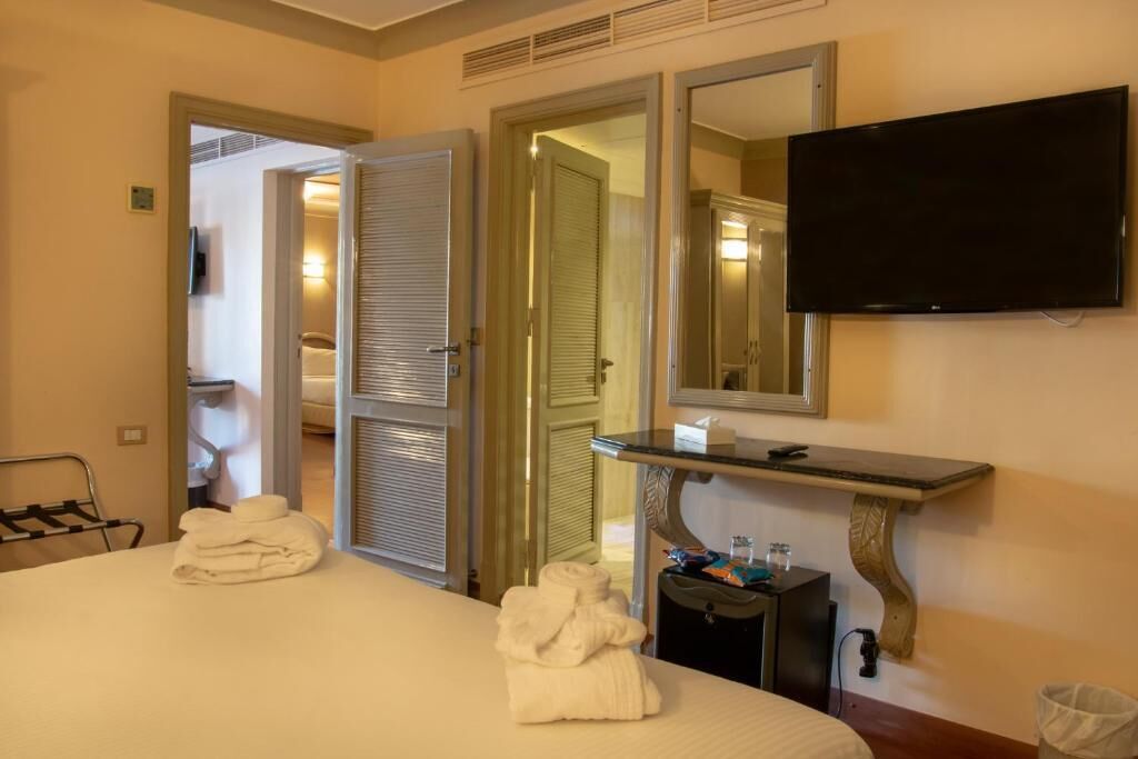 A hotel room with a bed, two towels, a TV, a mirror, and a small table with toiletries.