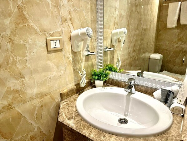Un baño con lavamanos de mármol, un espejo, un secador de pelo y una pequeña planta en maceta.