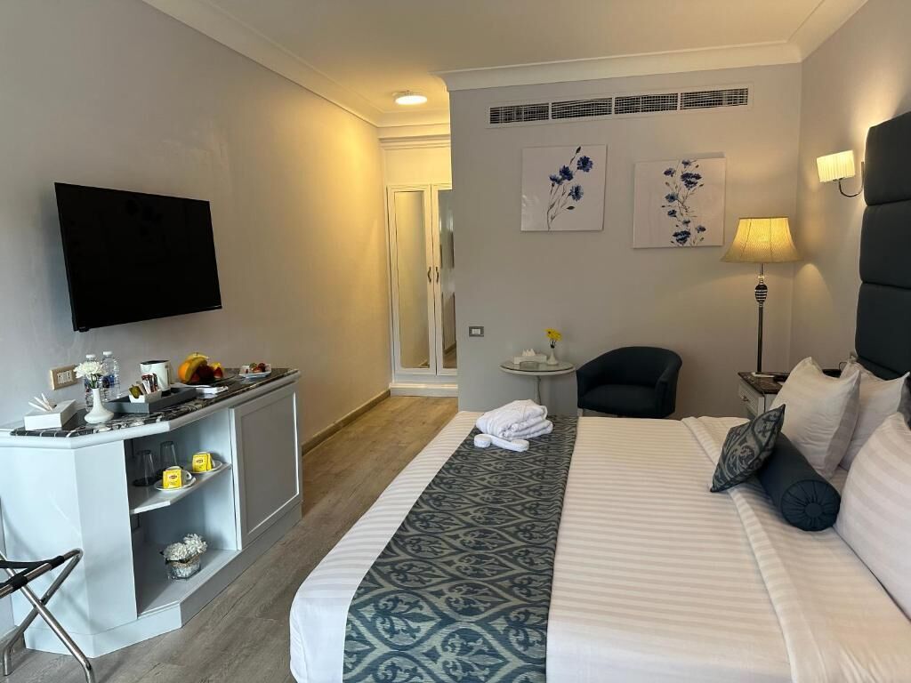Una habitación de hotel con una cama, un escritorio con televisor de pantalla plana, una silla y una lámpara.