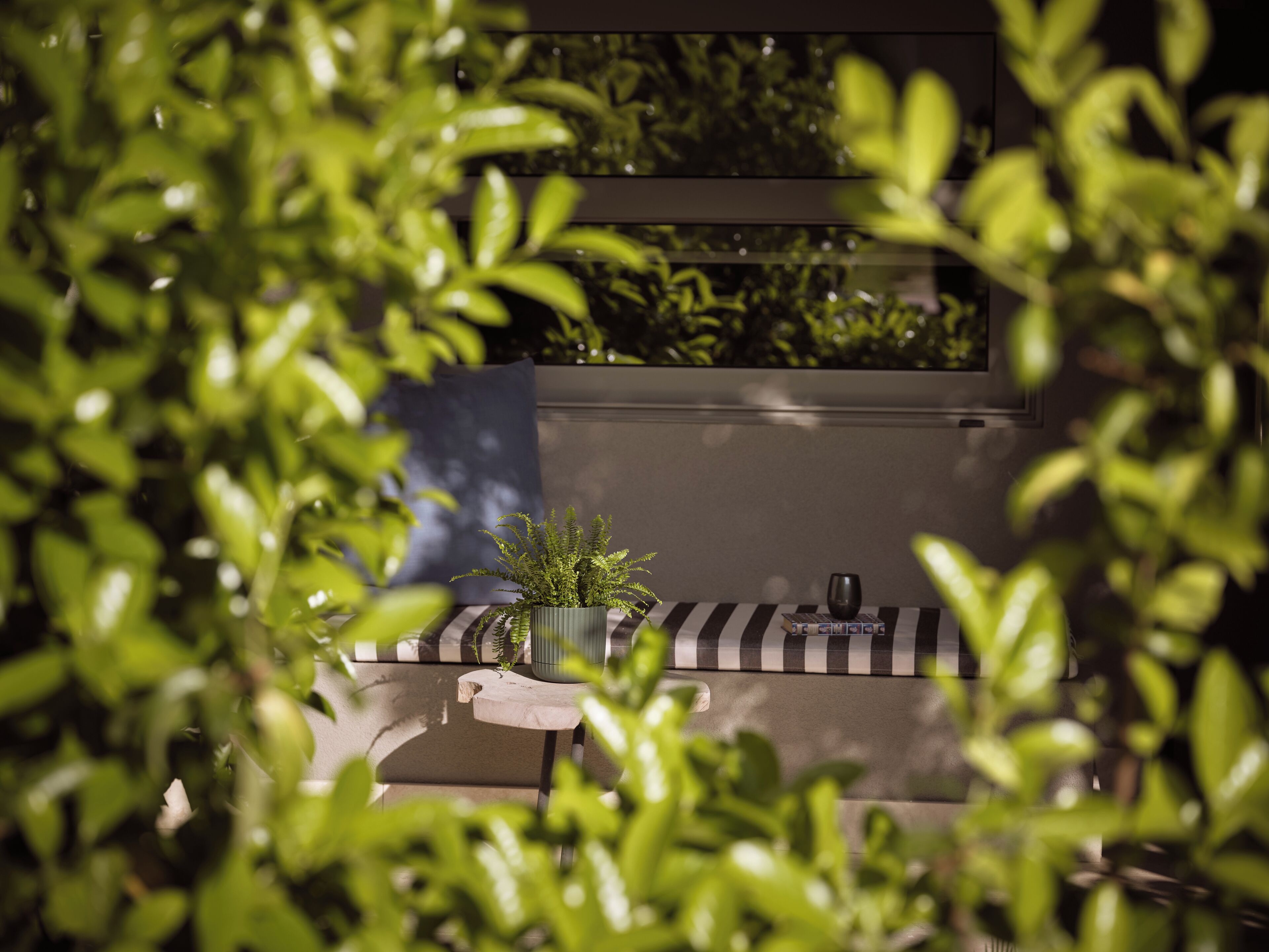 Un área de estar al aire libre moderna con una planta en maceta, una mesa a rayas y una silla oscura.