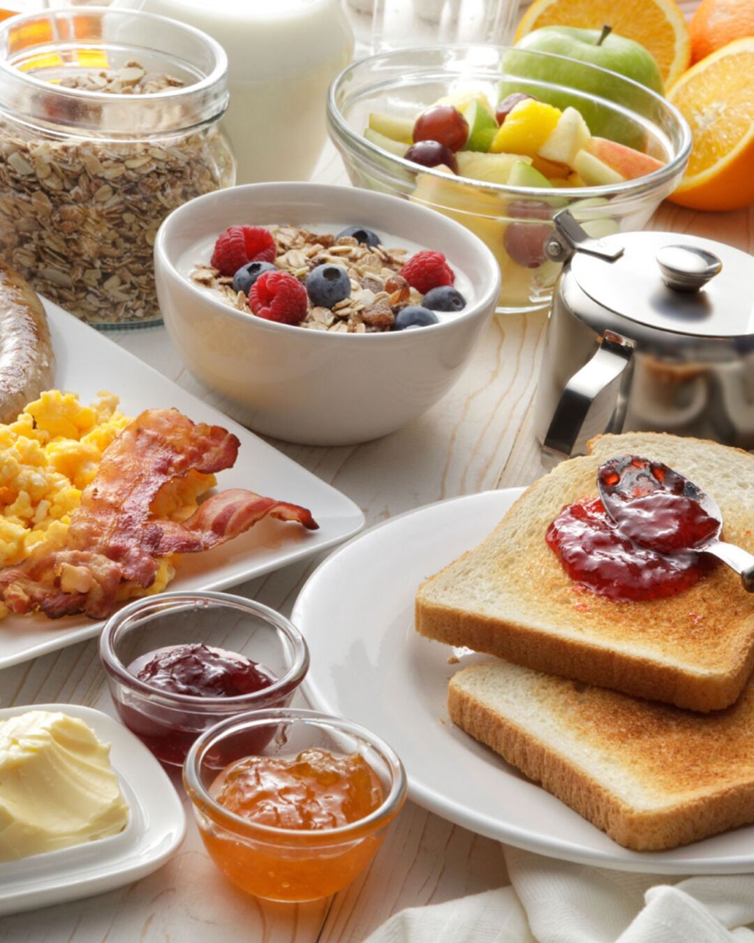 Desayuno con cereales, tostadas con mermelada, huevos revueltos, tocino y diferentes opciones para untar.