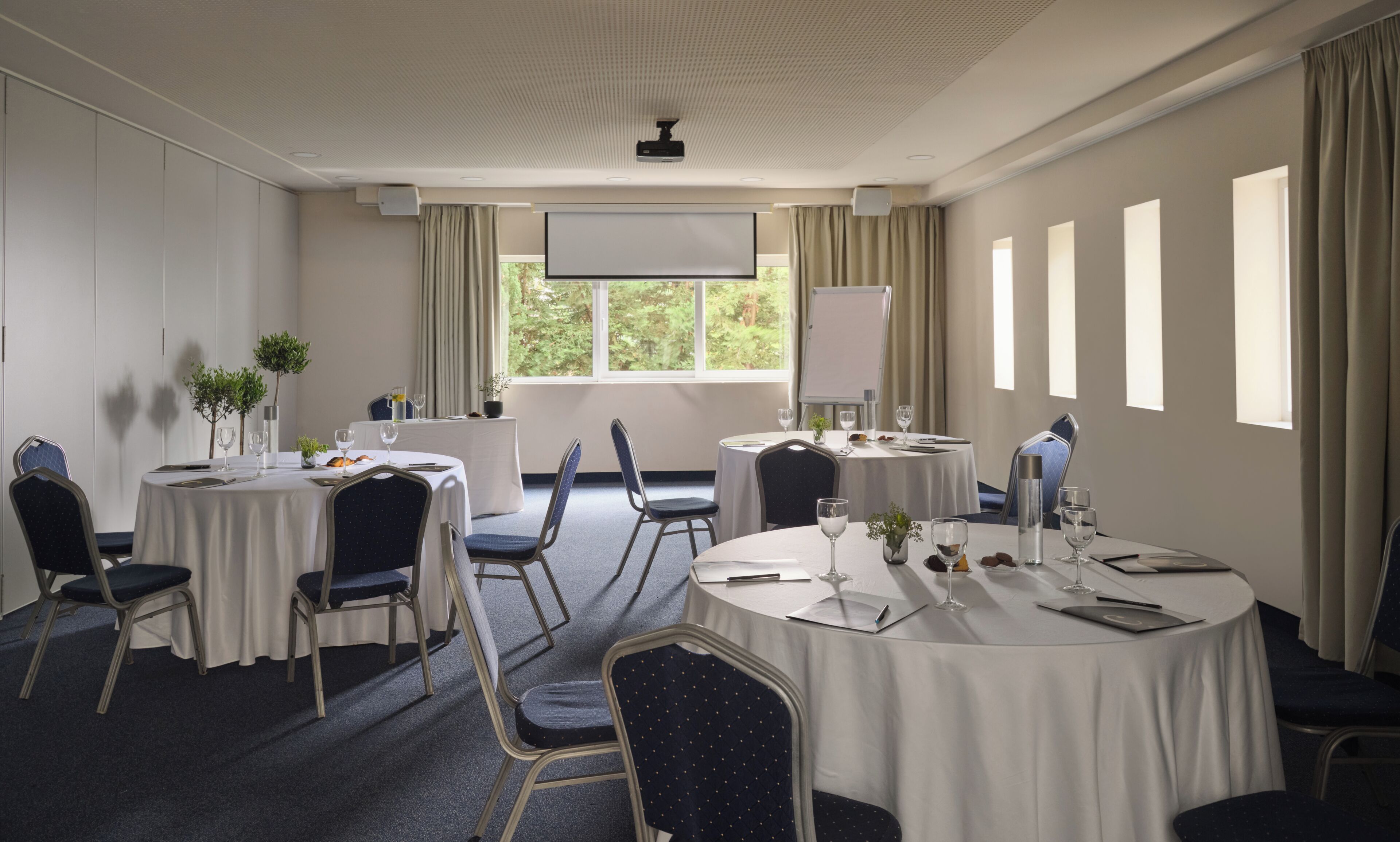 A conference room with round tables, chairs, a projector, and a whiteboard.