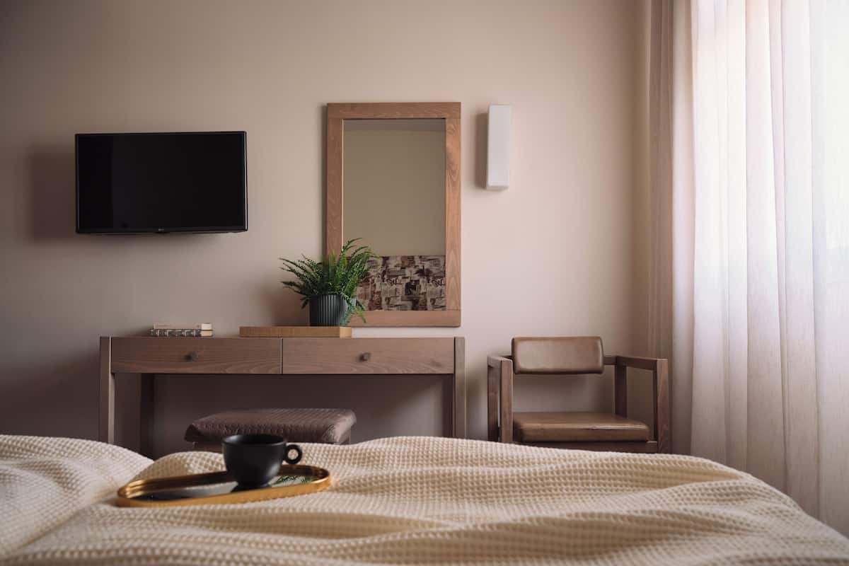 A bedroom with a bed, a bedside table, a television, a mirror, a chair, and a window with curtains.