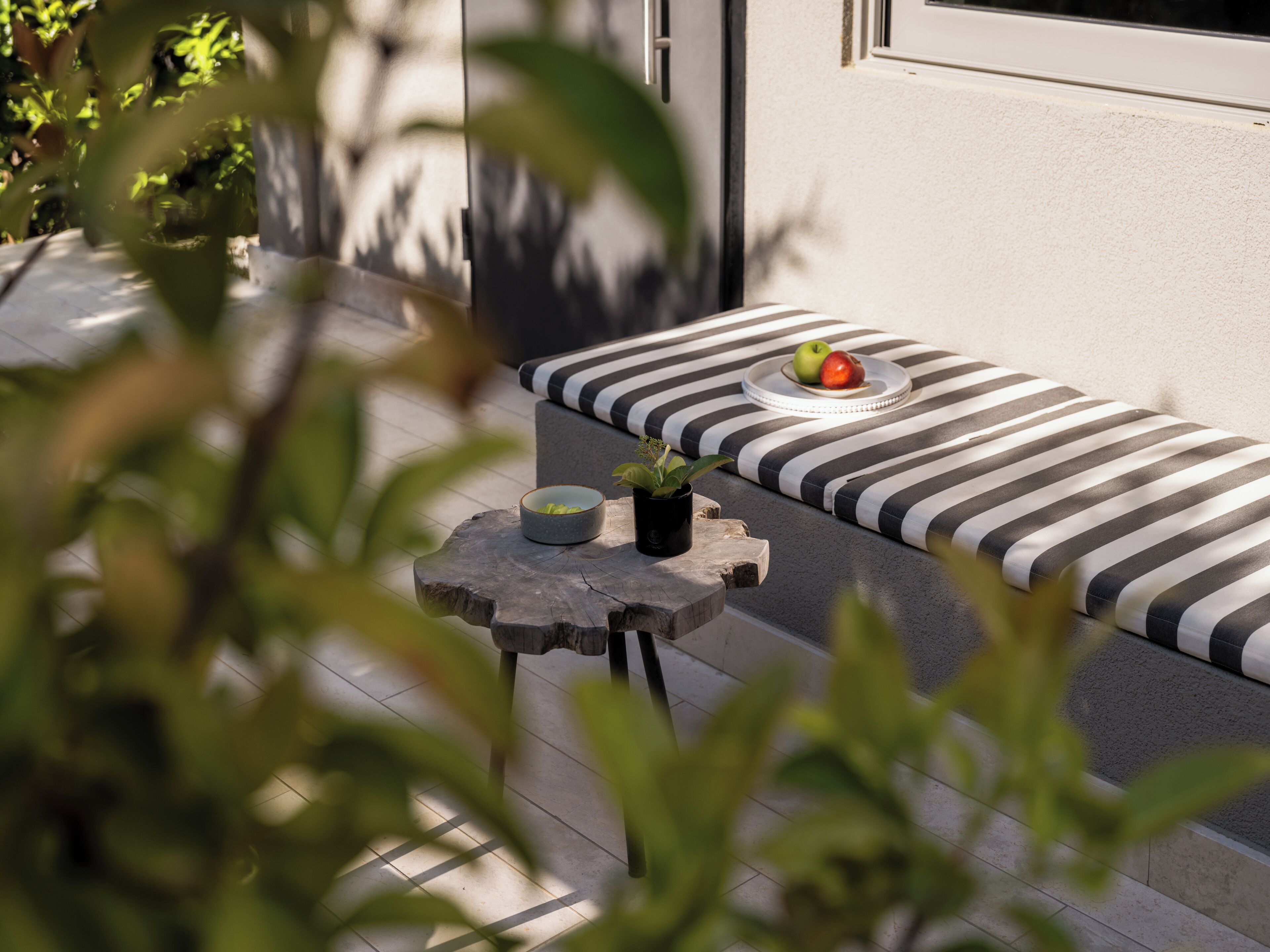 A modern outdoor seating area with a bench, a small table, and a potted plant.