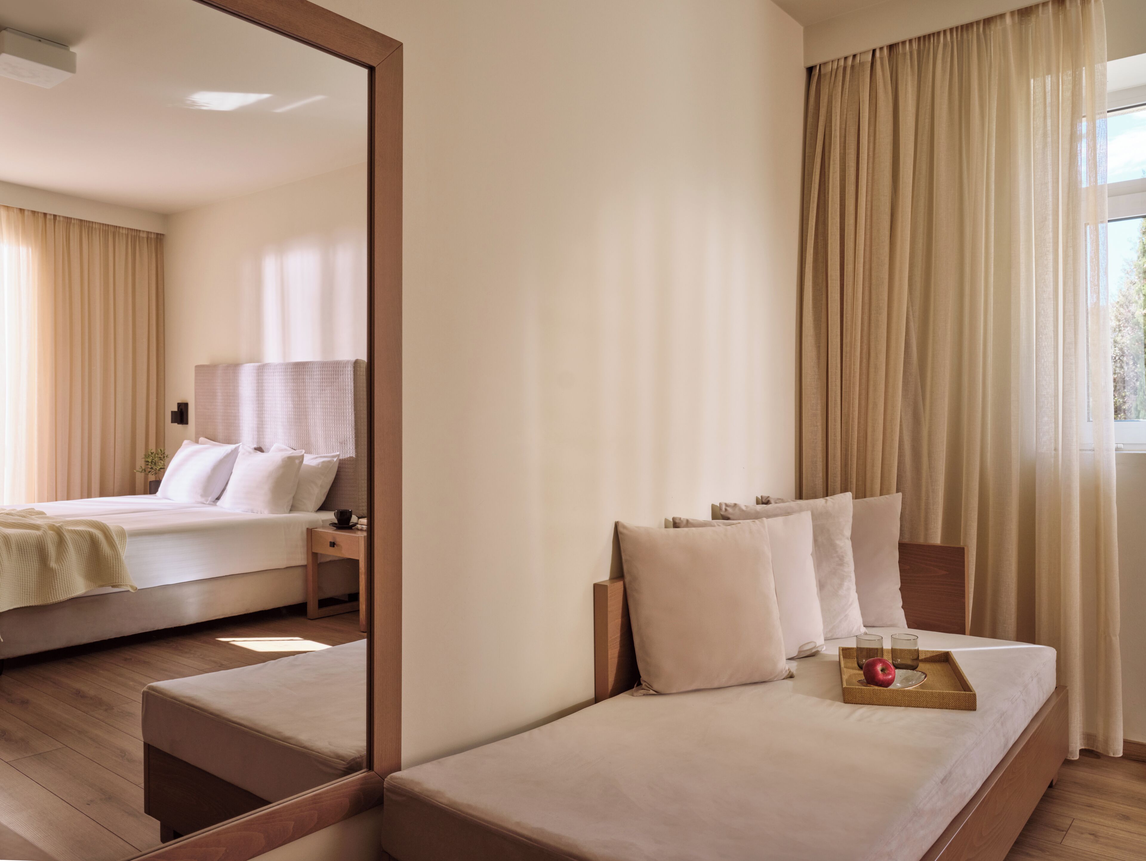 Une chambre d’hôtel avec un lit, une table de chevet, un miroir et une fenêtre avec des rideaux.