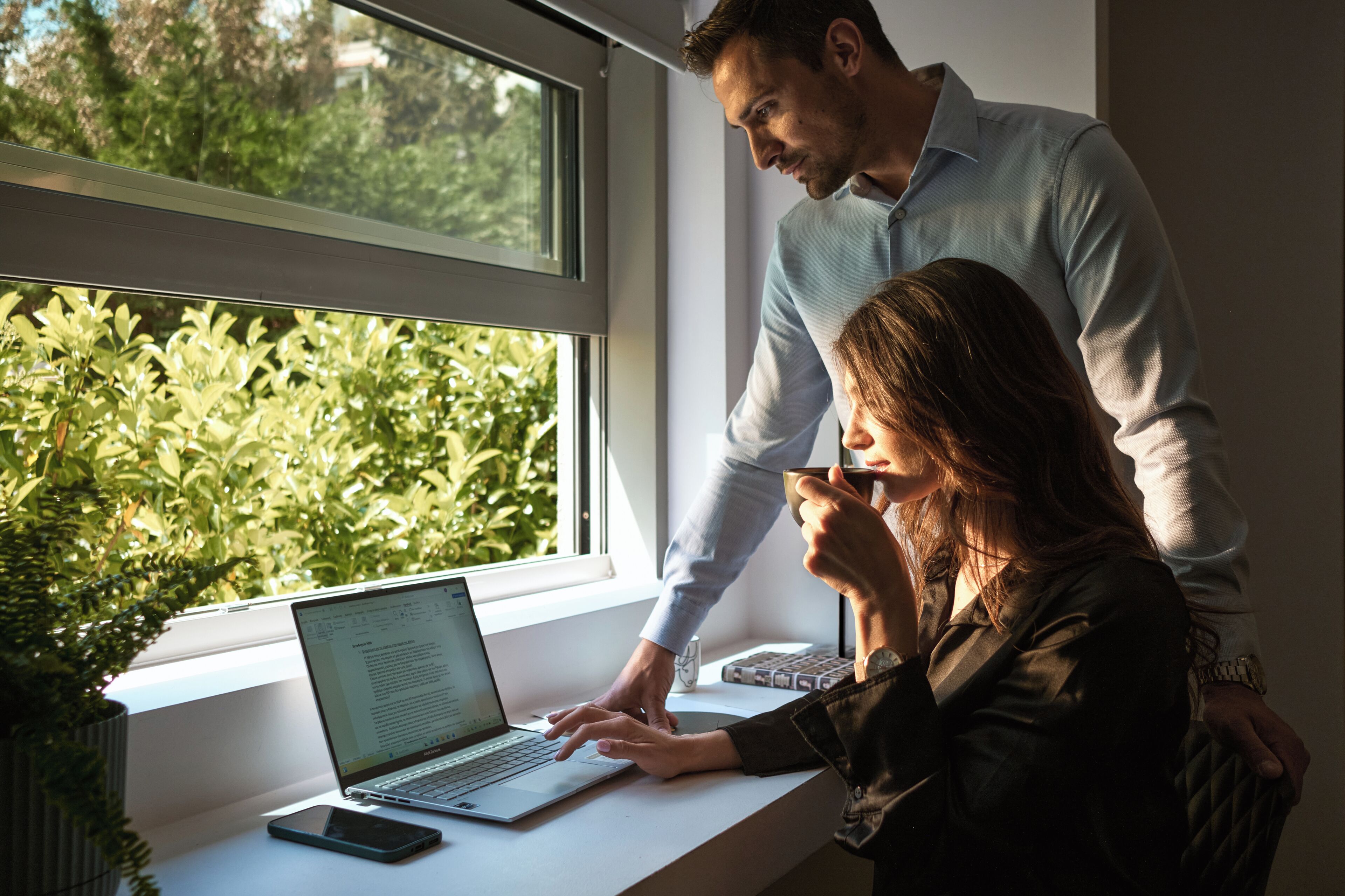 Une pièce comprenant un bureau, un ordinateur portable, un téléphone intelligent et une fenêtre donnant sur un paysage verdoyant.