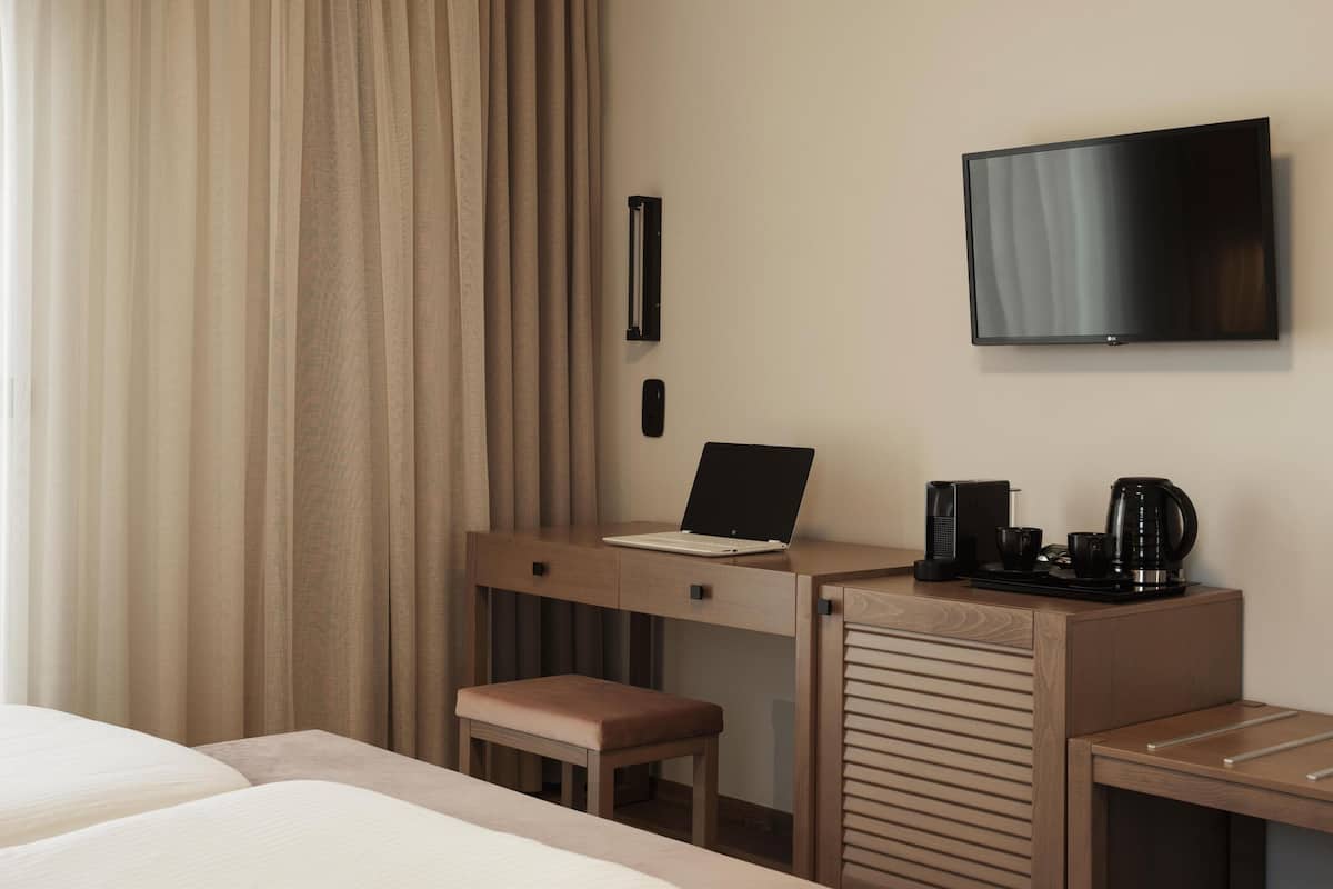 A hotel room with a bed, a desk with a laptop, a television, and a coffee maker.