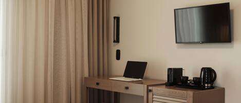 Una camera d'albergo con un letto, una scrivania con un portatile, una televisione e una macchina del caffè.