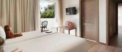 A hotel room with two beds, a TV mounted on the wall, a small table with a pink bag, and a window with curtains.