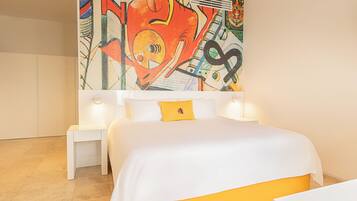 Habitación de hotel moderna con un cuadro abstracto grande en la pared, una cama blanca con un detalle amarillo y una mesita de noche pequeña.