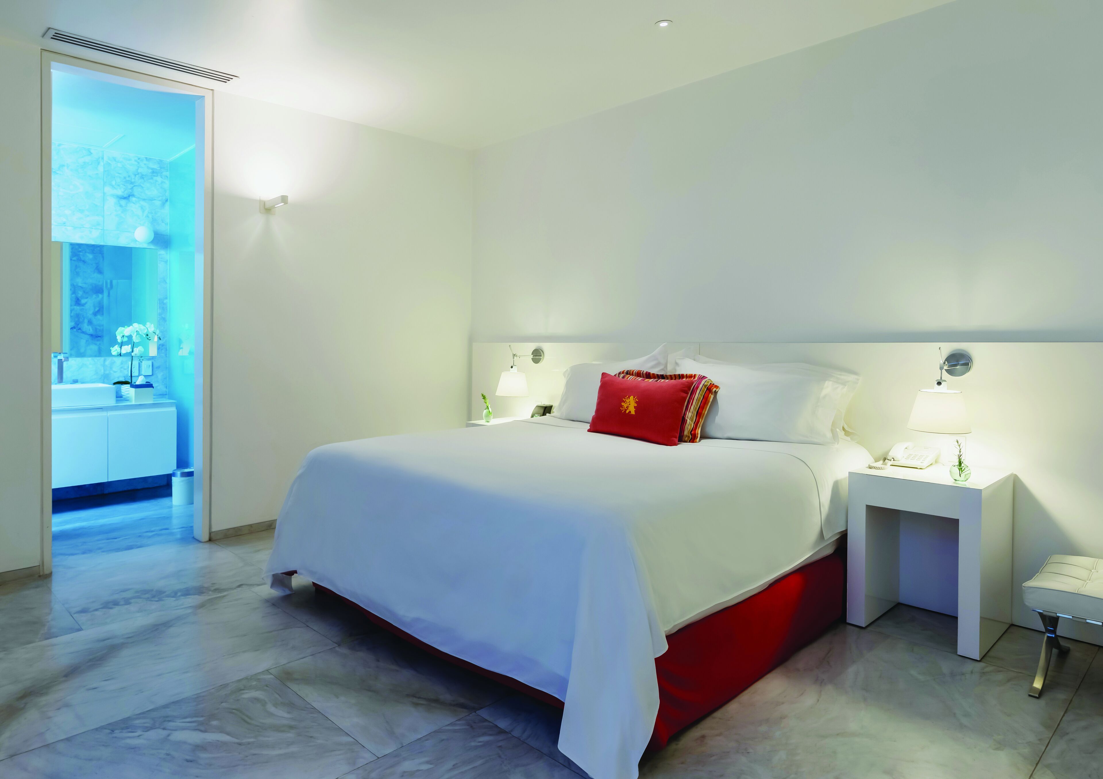 A hotel room with a large bed, white walls, and a bathroom visible through an open door.