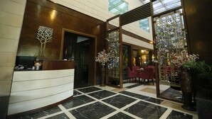 A lobby with a reception desk, a large vase with flowers, and a seating area with red chairs. - Hotel City Park Airport (New Delhi)