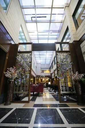 A hotel lobby with a high ceiling, skylight, and a checkered floor pattern. - Hotel City Park Airport (New Delhi)