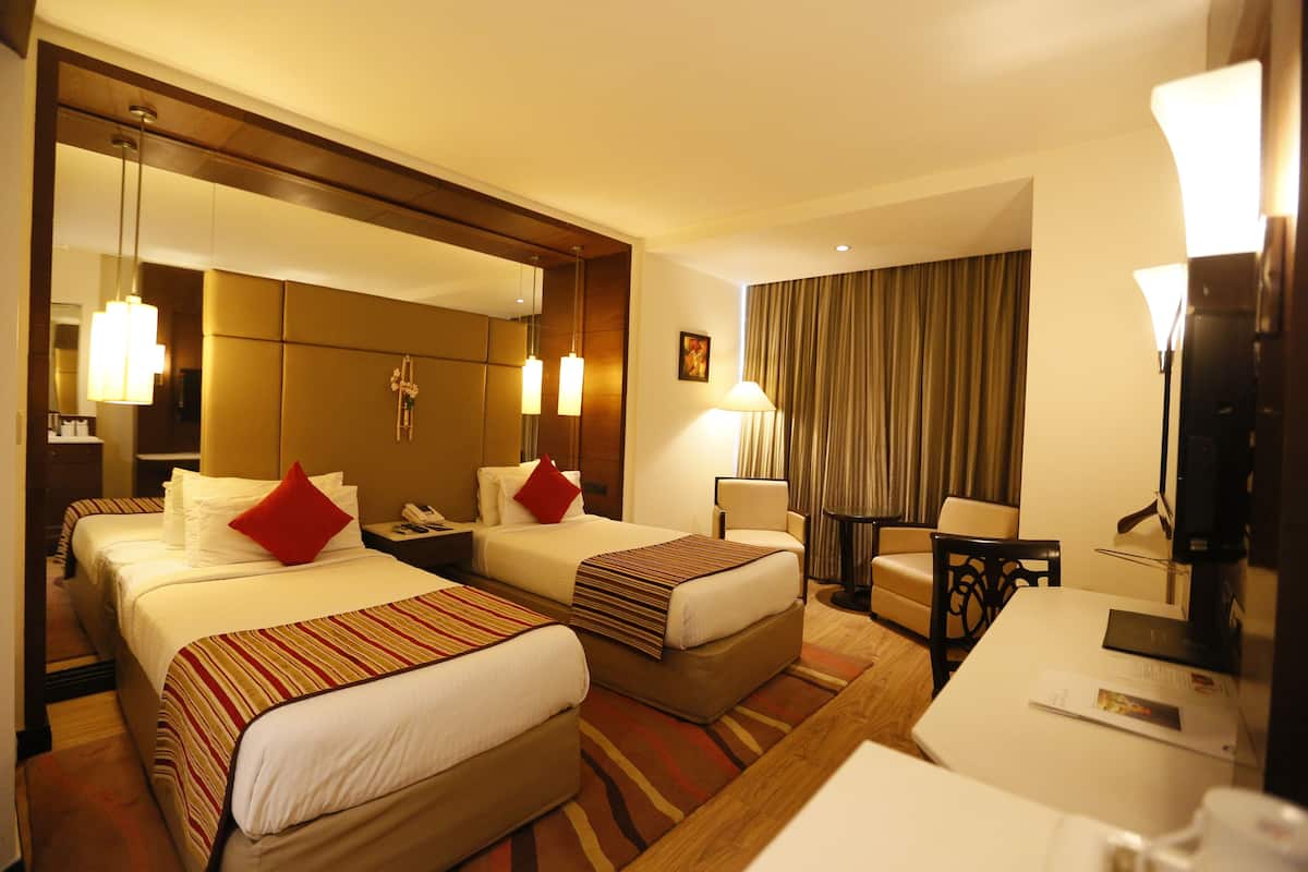 Habitación de hotel con dos camas, un escritorio, una silla, un televisor y un espejo grande.