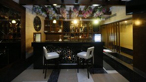 A bar area with two white cushioned bar stools, a black and white patterned wall, and hanging floral decorations. - Hotel City Park Airport (New Delhi)