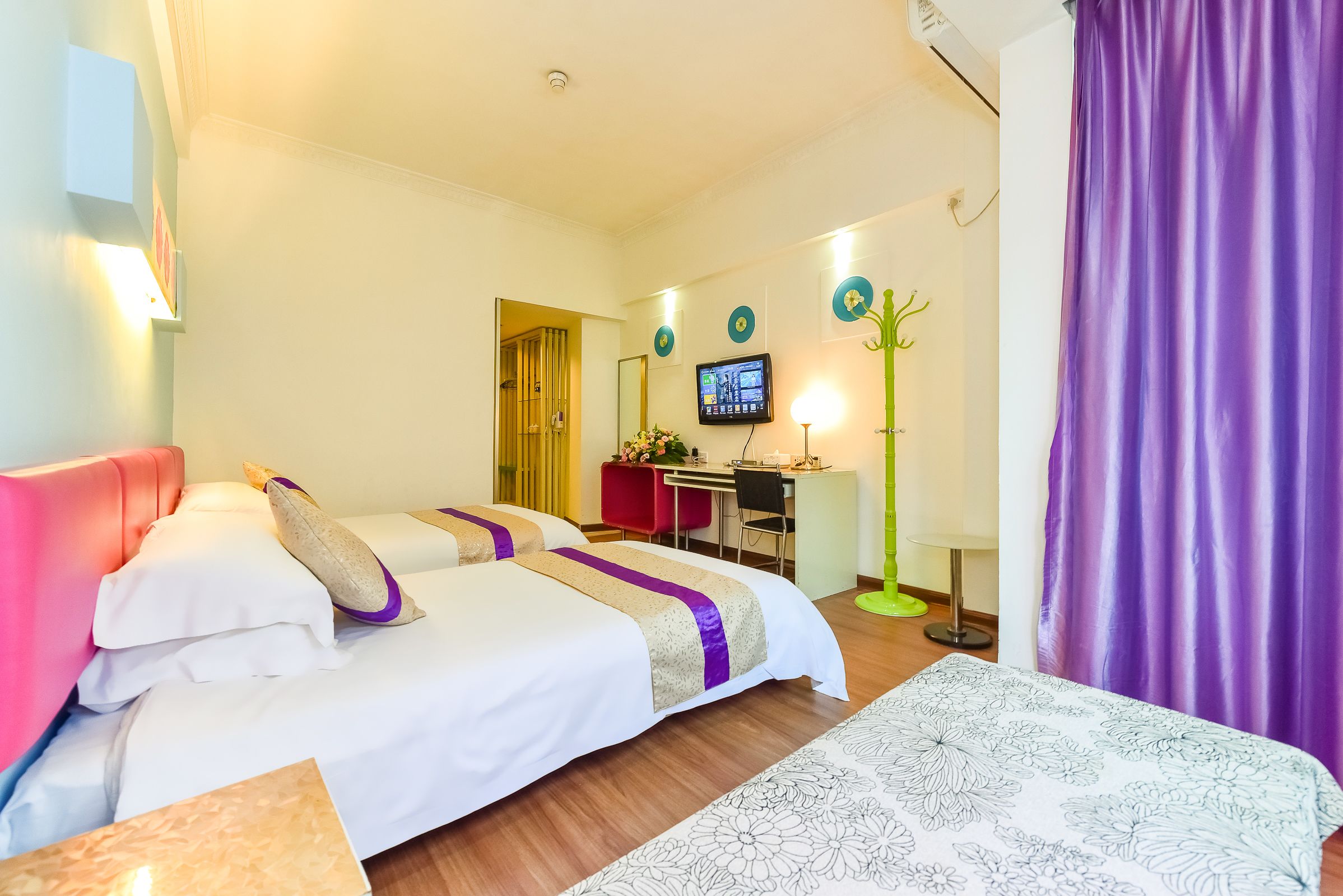 A hotel room with two beds, a desk, a television, and a window with curtains.