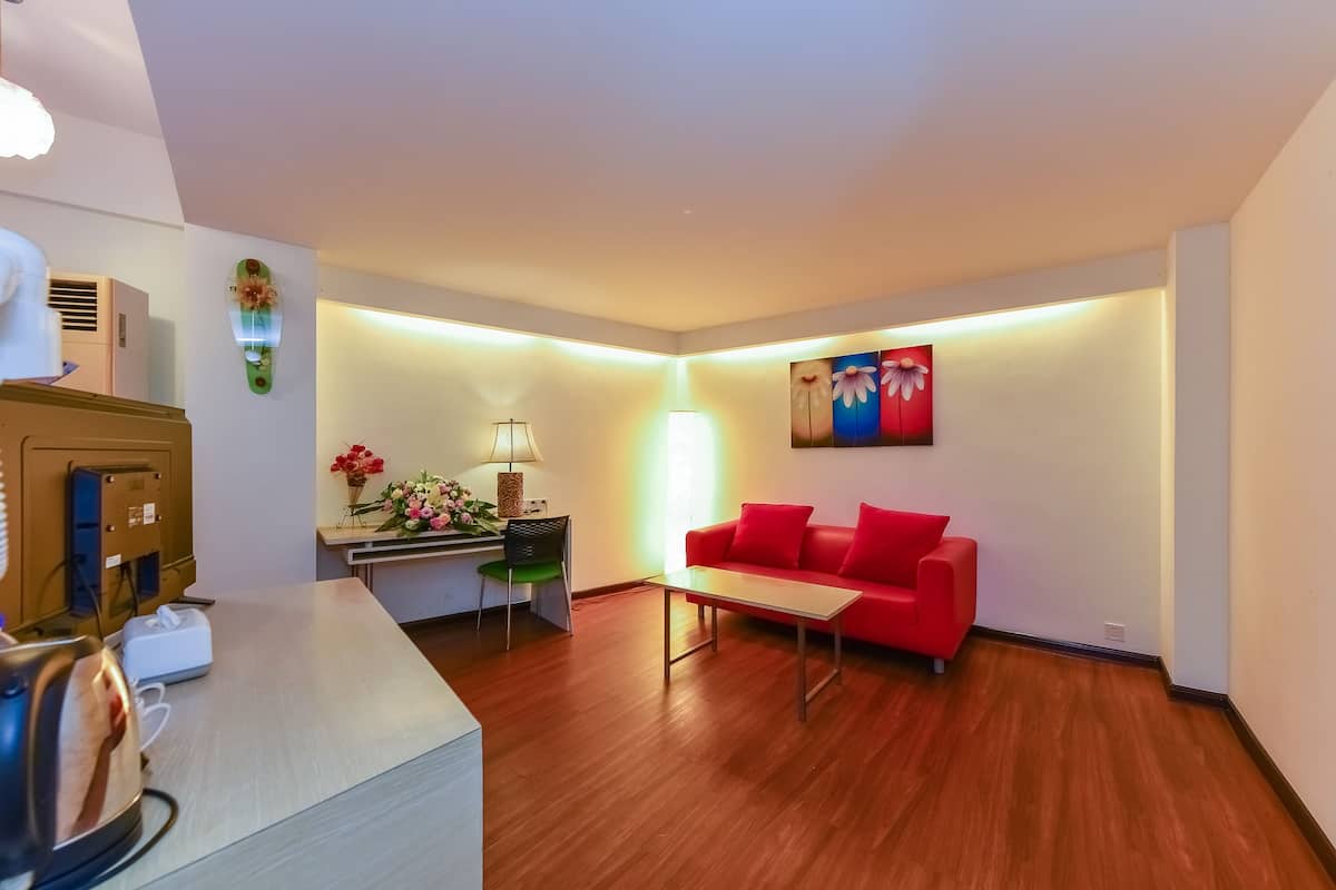 A modern living room with a red sofa, a coffee table, a desk with a lamp, and a wall-mounted artwork.